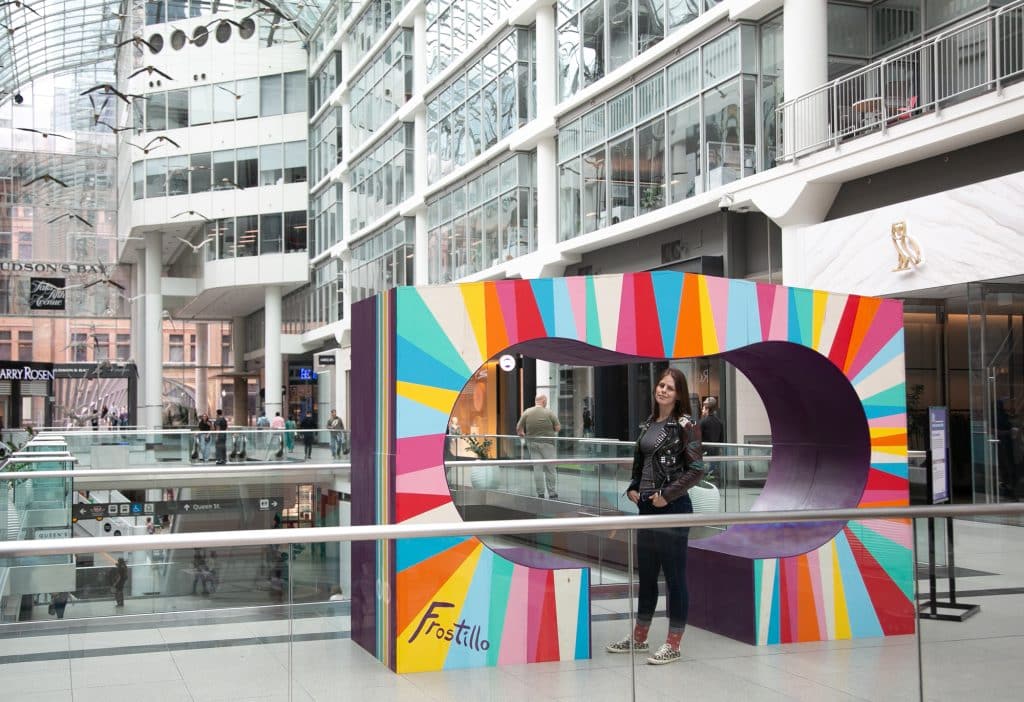 a person stands under an arch-like sculpture in a mall